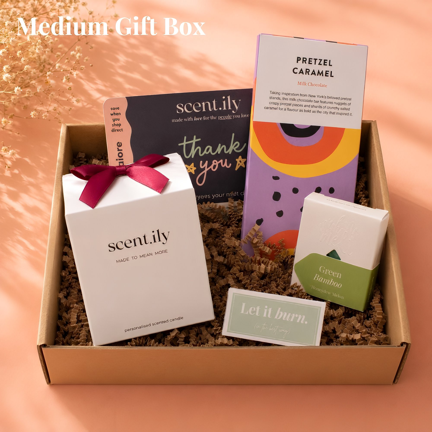 A medium-sized gift box containing various items, including a scented candle, a chocolate bar, and a card.