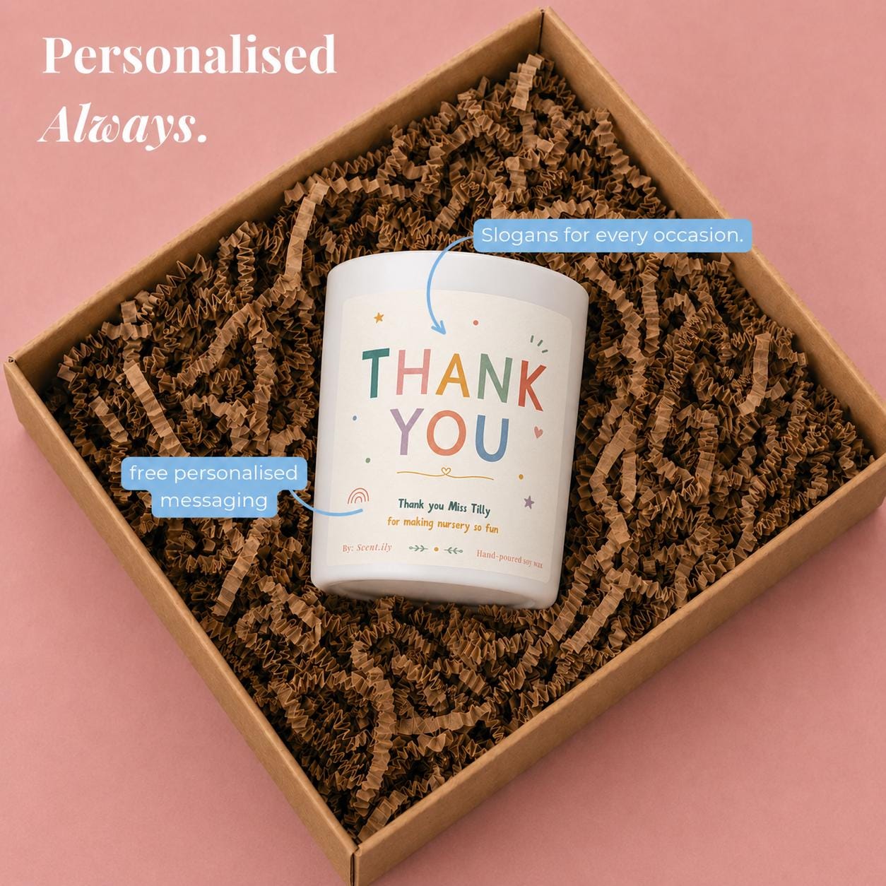 A white candle with a colorful design and text that says "Thank You" is placed in a cardboard box filled with brown paper shavings.