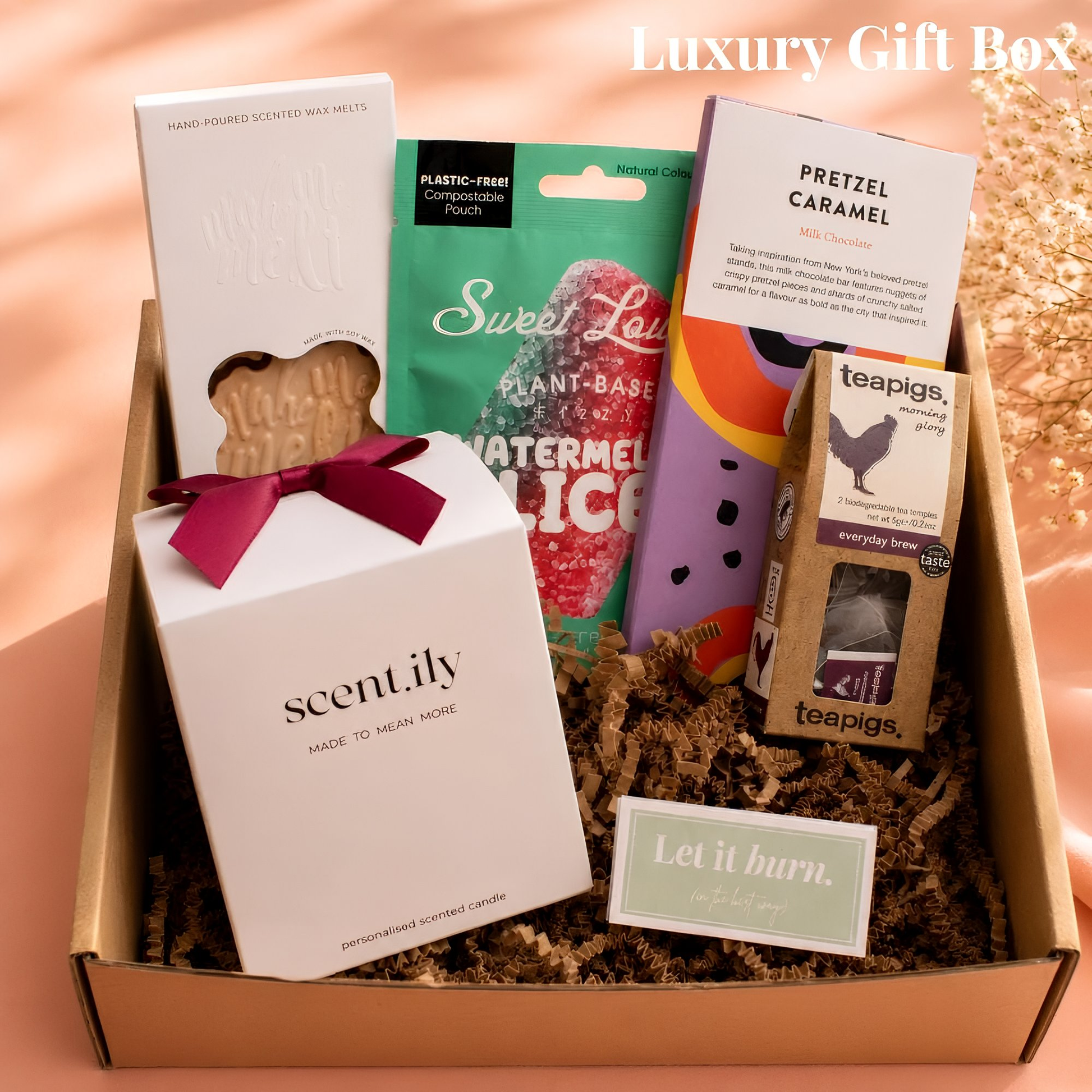 A gift box containing various items, including a hand-poured scented wax melts, a sweet lime, a pretzel, a tea bag, and a card.
